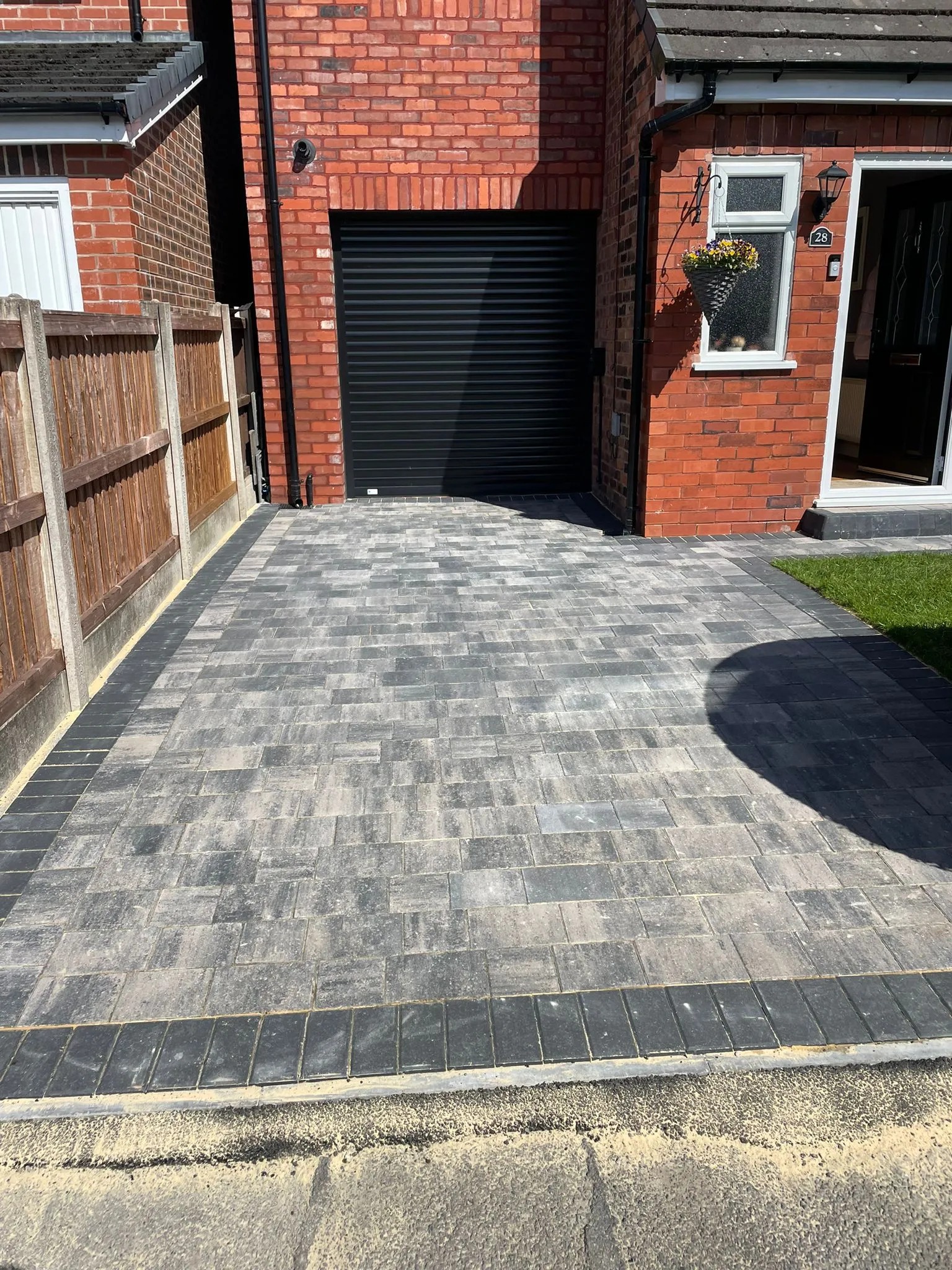 Grey block-paved driveway beside a red-brick house laid by T&T Driveways